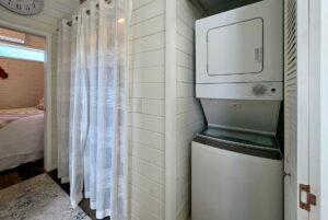 Stacked washer and dryer in a cozy laundry nook at 47 Drifting Brook, next to a bedroom with white shiplap walls.