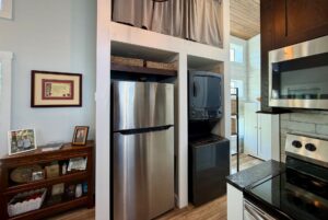 Stainless steel fridge and stacked washer-dryer in a modern kitchen at 106 Meandering Lane with wood and white accents.