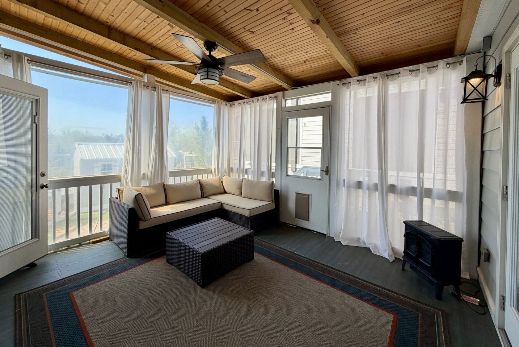 Screened-in porch at 53 Highland Hill with a sectional sofa, ottoman, ceiling fan, sheer curtains, and wood ceiling.