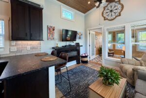Cozy living area at 106 Meandering Lane with TV, bar stools, black cabinets, wall art, and glass doors to a sunroom.
