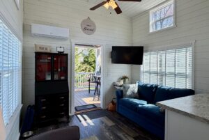 Cozy living room at 47 Drifting Brook with blue sofa, TV, large windows, and door opening to a sunny deck with seating.