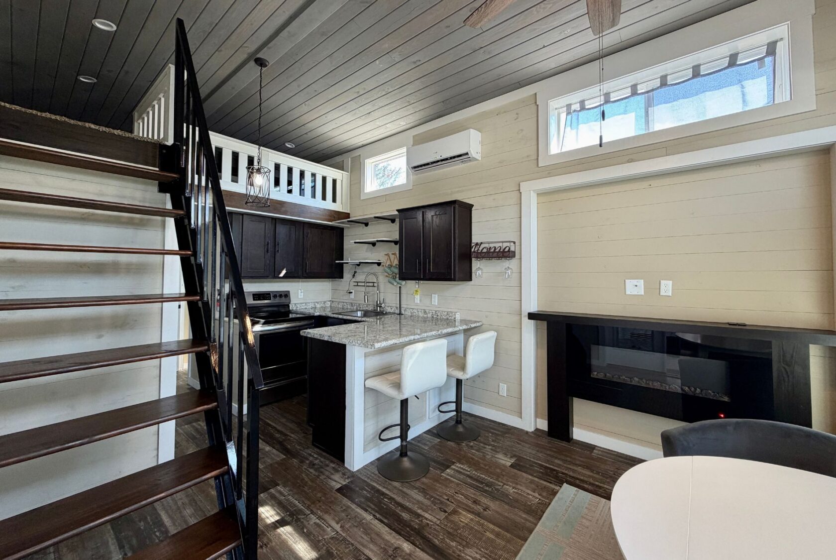 Modern tiny house interior at 53 Highland Hill Lane with loft, dark wood kitchen, granite island, and spiral staircase.