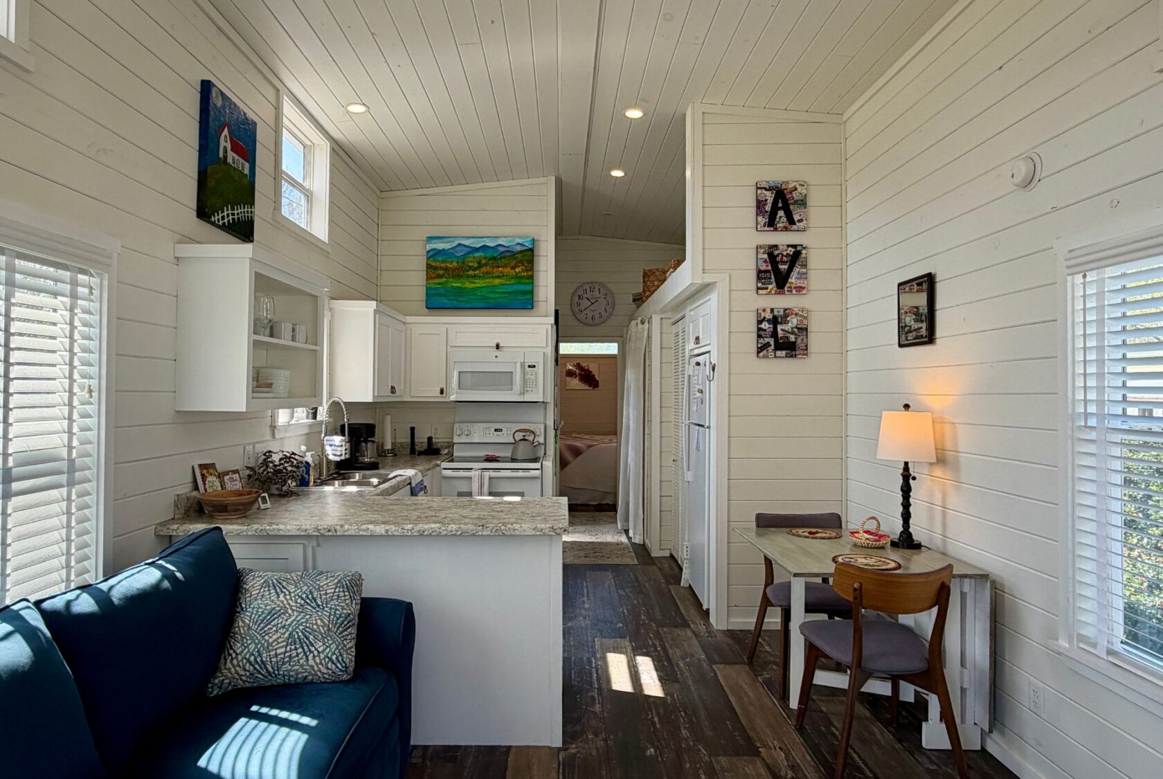 Bright, cozy tiny house on 47 Drifting Brook with white walls, kitchen, dining area, couch, and colorful wall art.