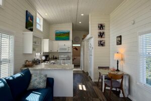Bright, cozy tiny house on 47 Drifting Brook with white walls, kitchen, dining area, couch, and colorful wall art.