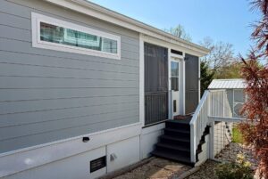 Light gray mobile home on Highland Hill Lane with a small porch, white railing, and stairs to the entrance.