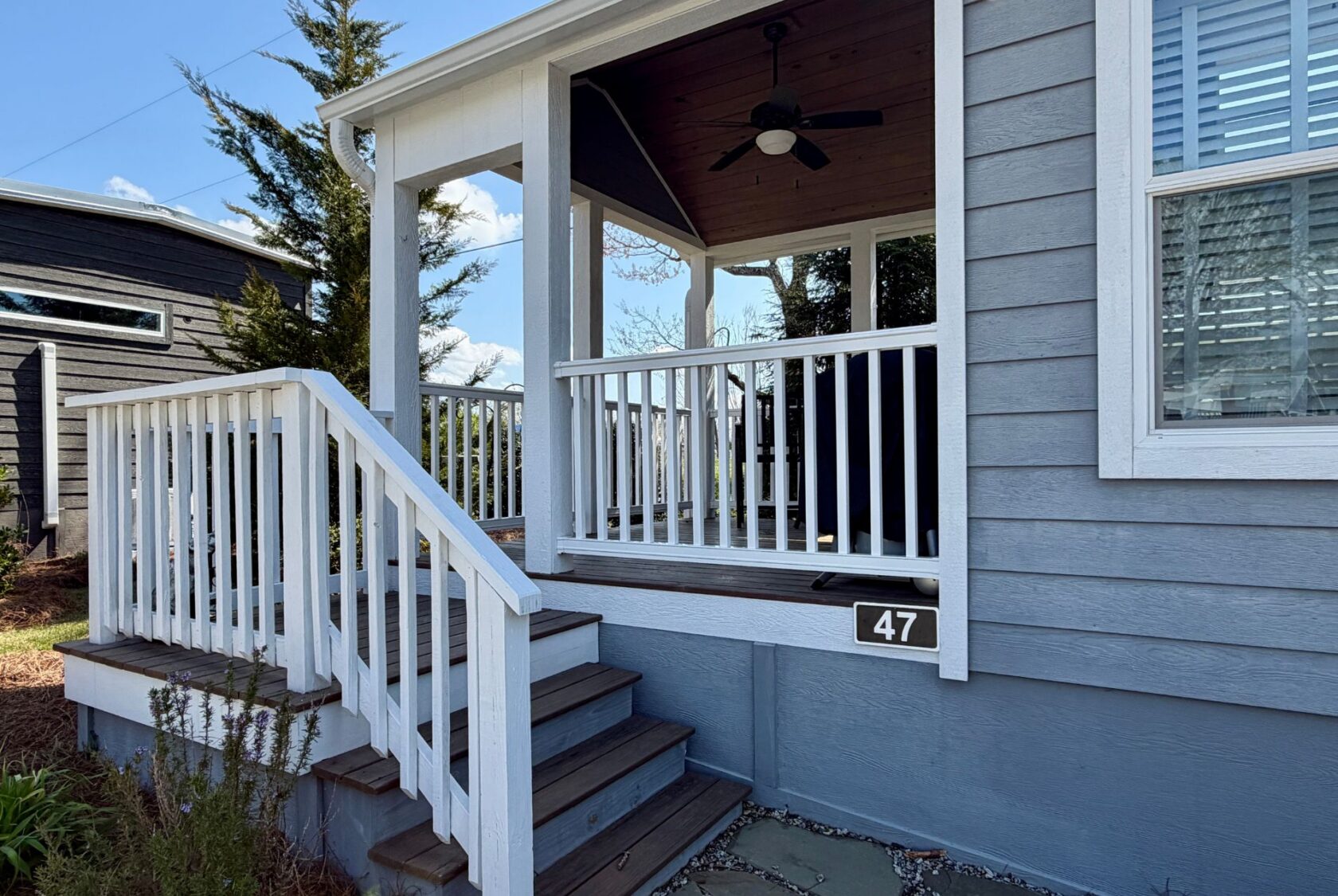 Gray house with white trim at 47 Drifting Brook Lane features a front porch, steps, railing, and number sign by the entrance.