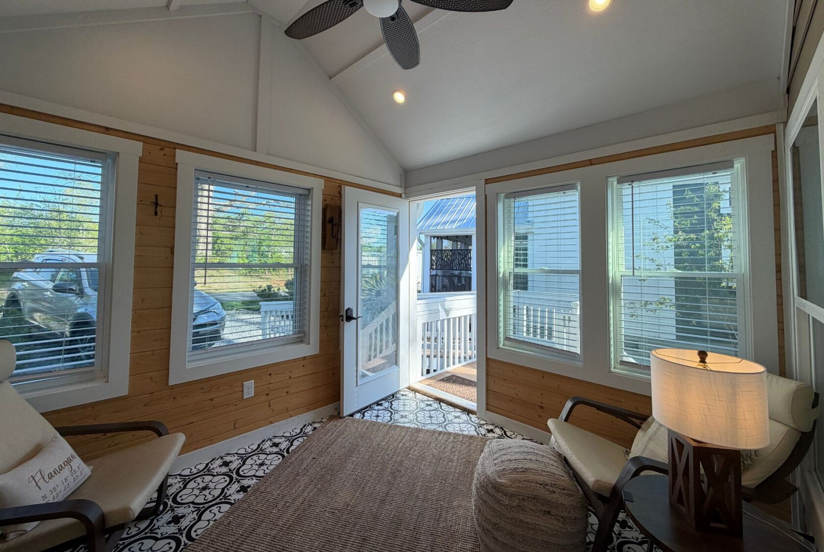 Bright sunroom at 106 Meandering Lane with large windows, armchairs, and open doors leading to an outdoor deck.