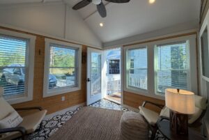 Bright sunroom at 106 Meandering Lane with large windows, armchairs, and open doors leading to an outdoor deck.