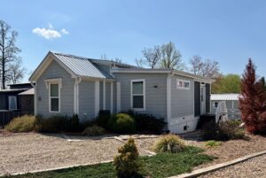 Charming small light blue house with metal roof on Highland Hill Lane, surrounded by gravel and shrubs.