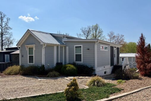 Charming small light blue house with metal roof on Highland Hill Lane, surrounded by gravel and shrubs.