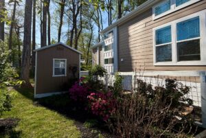 A small shed and flowering bushes beside a beige house with large windows at 106 Meandering Lane real estate.