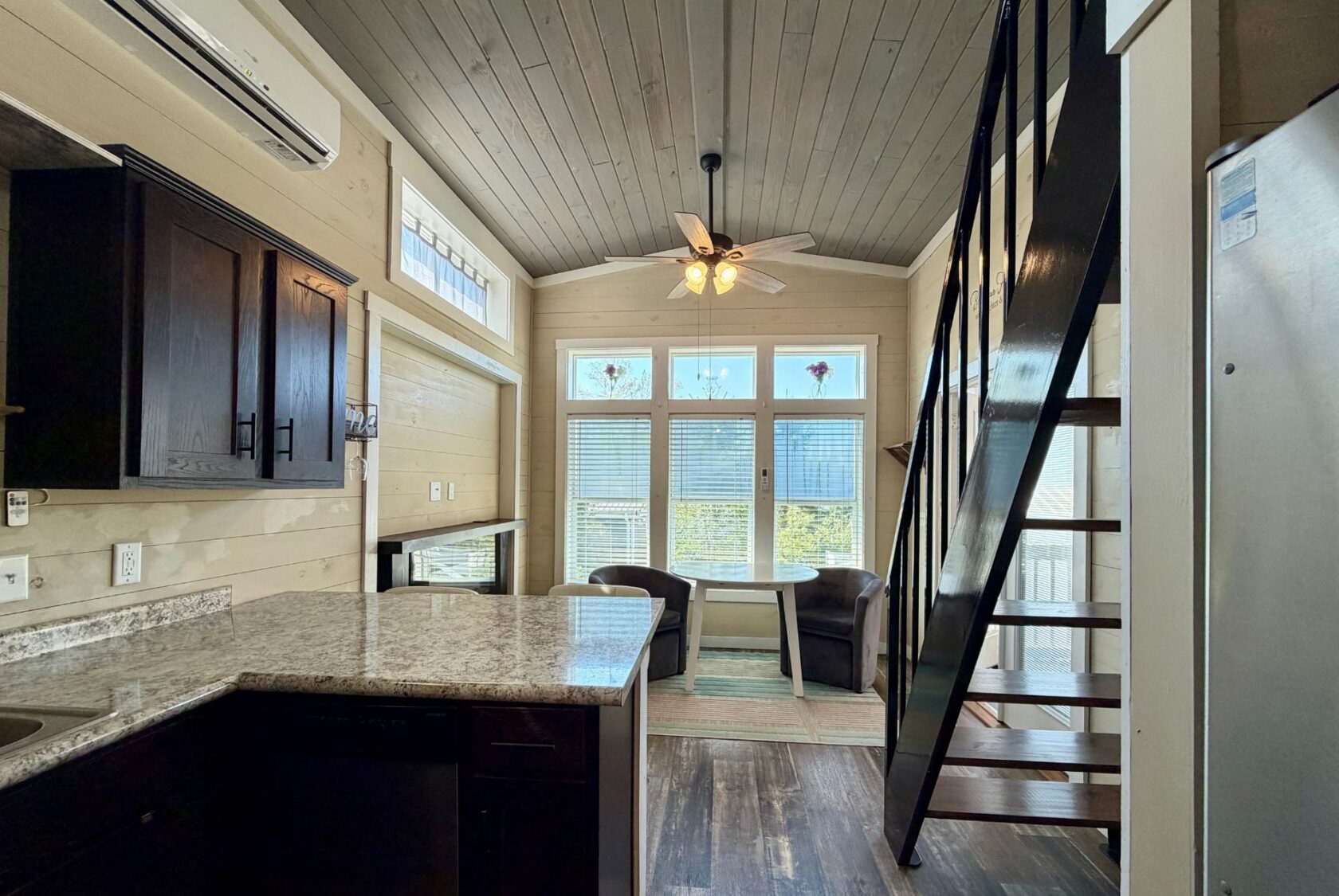 Tiny house interior on Highland Hill Lane with a kitchen, dining nook by large windows, and a loft staircase.