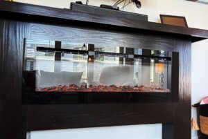 Modern electric fireplace with glowing embers on Meandering Lane, set in a dark wooden mantle for a cozy living room feel.