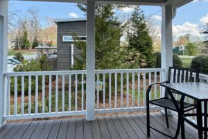 A porch at 47 Drifting Brook with a black table and chairs overlooks a garden and modern building in this real estate gem.