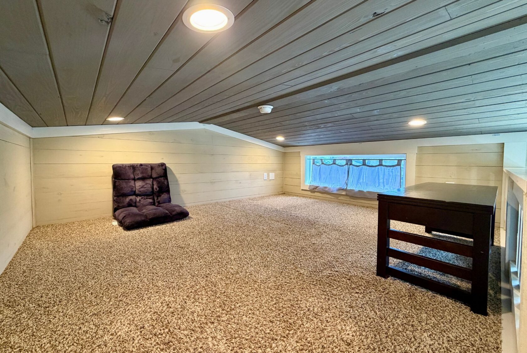 Cozy loft at 53 Highland Hill Lane with carpet, a floor chair, small table, and curtained window under wooden ceiling.