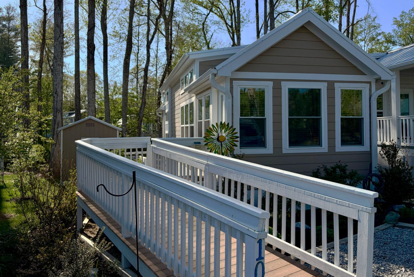 A tan house with white trim at 106 Meandering Lane, featuring a ramp and trees in the background on a sunny day.