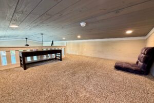 Cozy loft space at 53 Highland Hill Lane with a black desk, floor chair, carpet flooring, and wood-paneled ceiling with lights.
