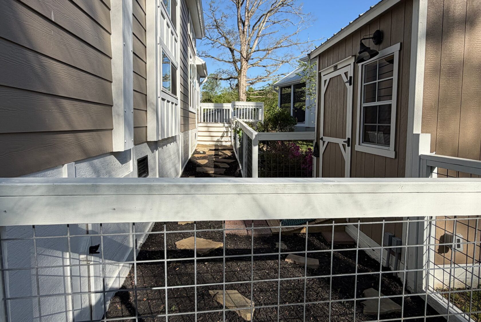 Narrow fenced pathway at 106 Meandering Lane with a stone path, leading to stairs and a wooden deck.