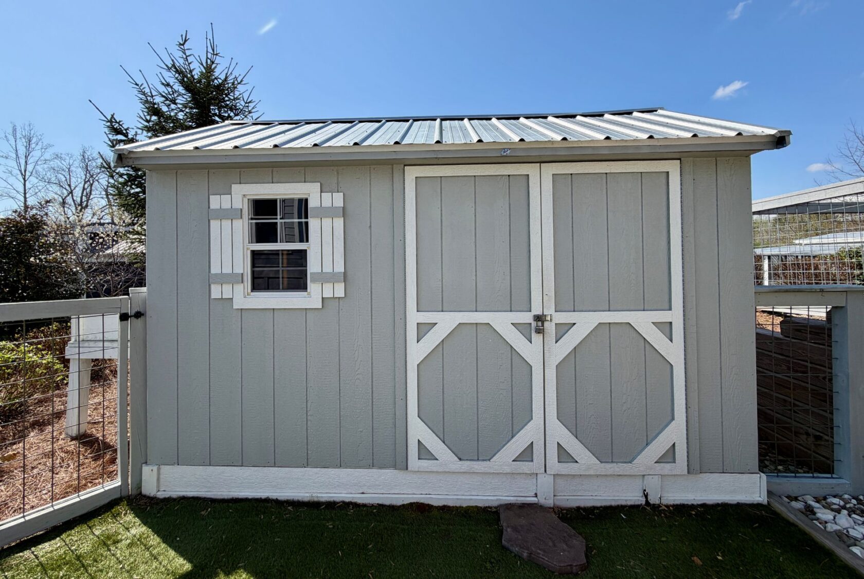 Light gray garden shed with double doors, nestled in the fenced yard of 53 Highland Hill real estate.