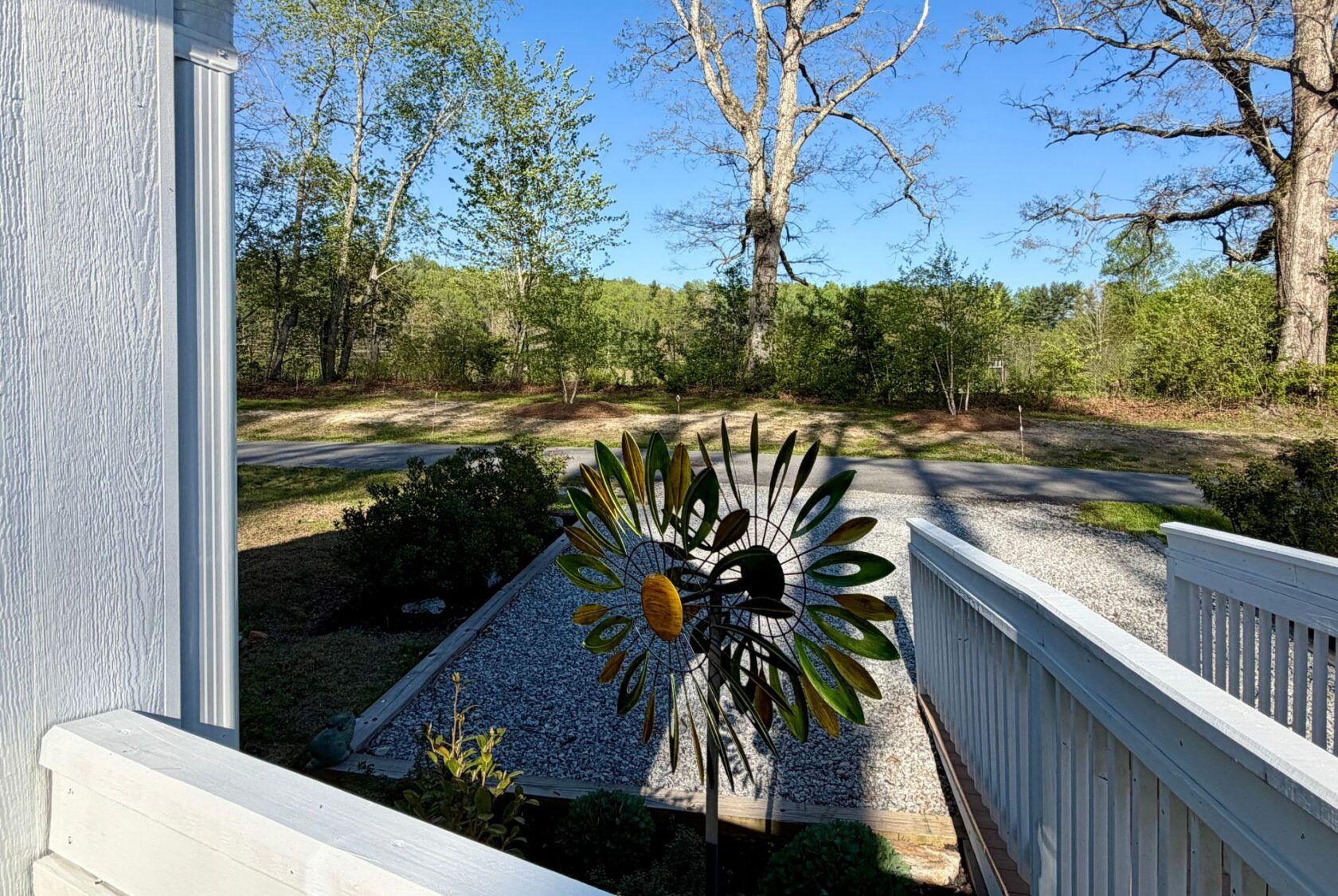 A colorful metal sunflower garden spinner brightens the gravel drive at 106 Meandering Lane under clear blue skies.