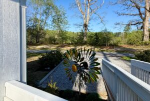 A colorful metal sunflower garden spinner brightens the gravel drive at 106 Meandering Lane under clear blue skies.