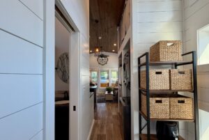 Hallway of a modern tiny house at 106 Meandering Lane with wood floors, basket shelves, and large window views.