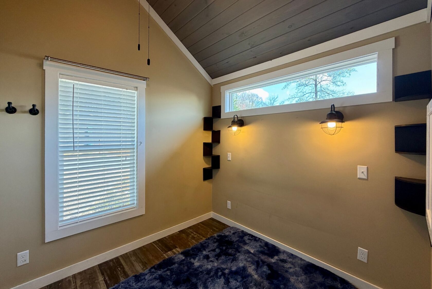 Small room at 53 Highland Hill Lane with beige walls, wood ceiling, wall lights, shelves, blinds, and a blue rug.