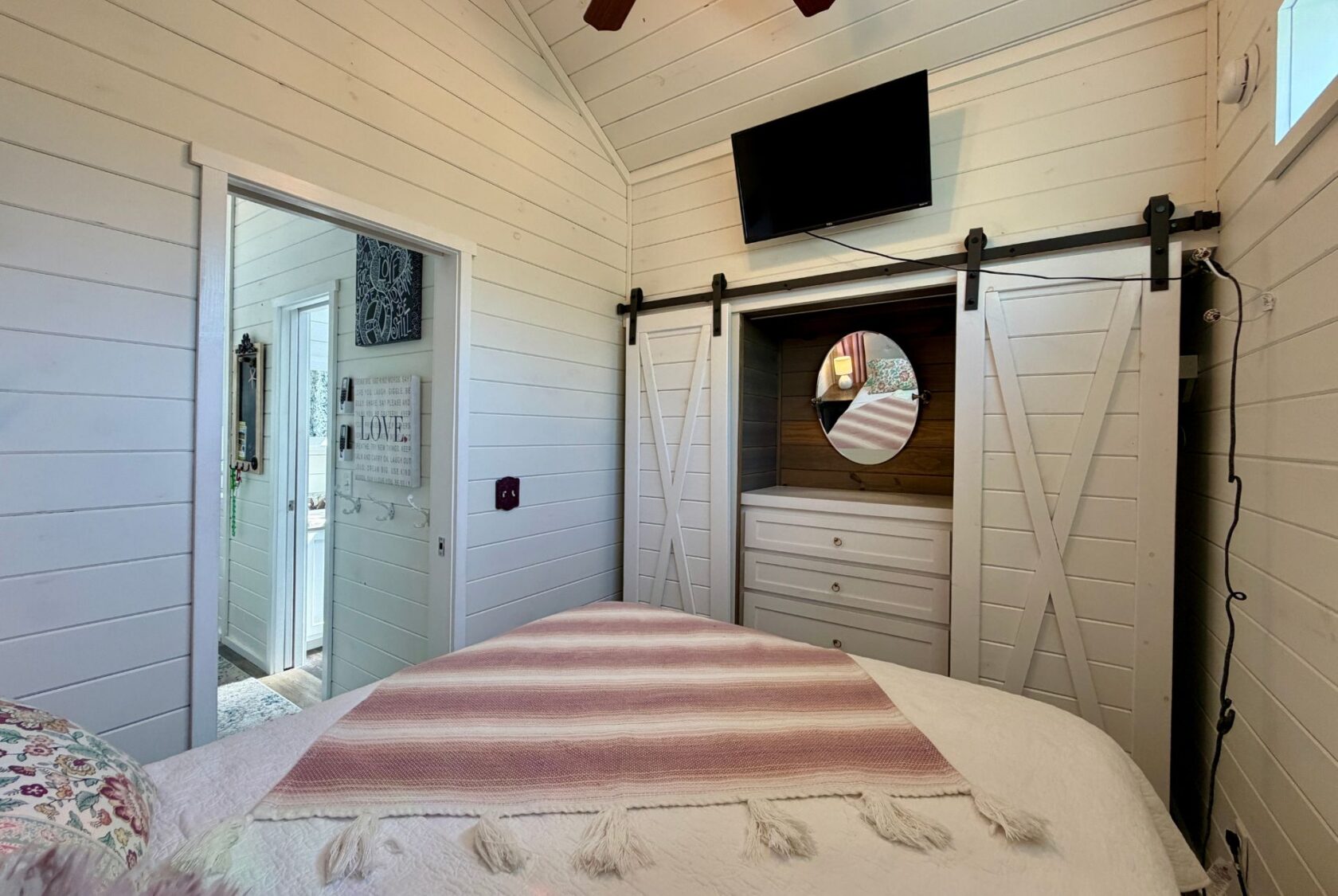 Cozy bedroom at 47 Drifting Brook with white shiplap walls, barn doors, TV, and a pink-striped blanket on the bed.