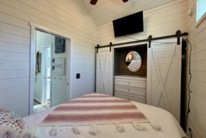 Cozy bedroom at 47 Drifting Brook with white shiplap walls, barn doors, TV, and a pink-striped blanket on the bed.