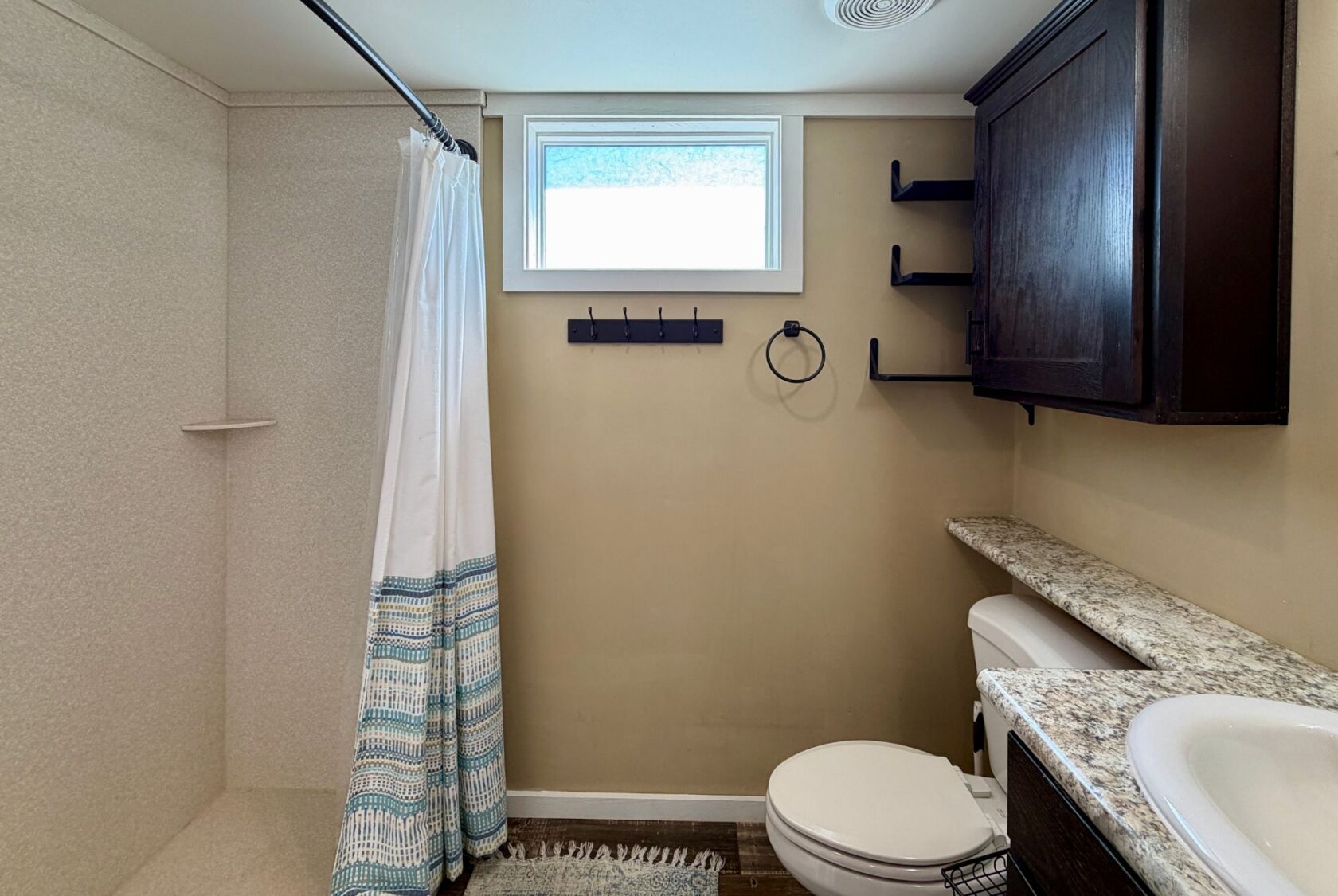 Bathroom with shower, white curtain, shelves, window, and granite sink at 53 Highland Hill.