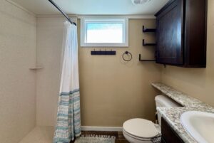 Bathroom with shower, white curtain, shelves, window, and granite sink at 53 Highland Hill.