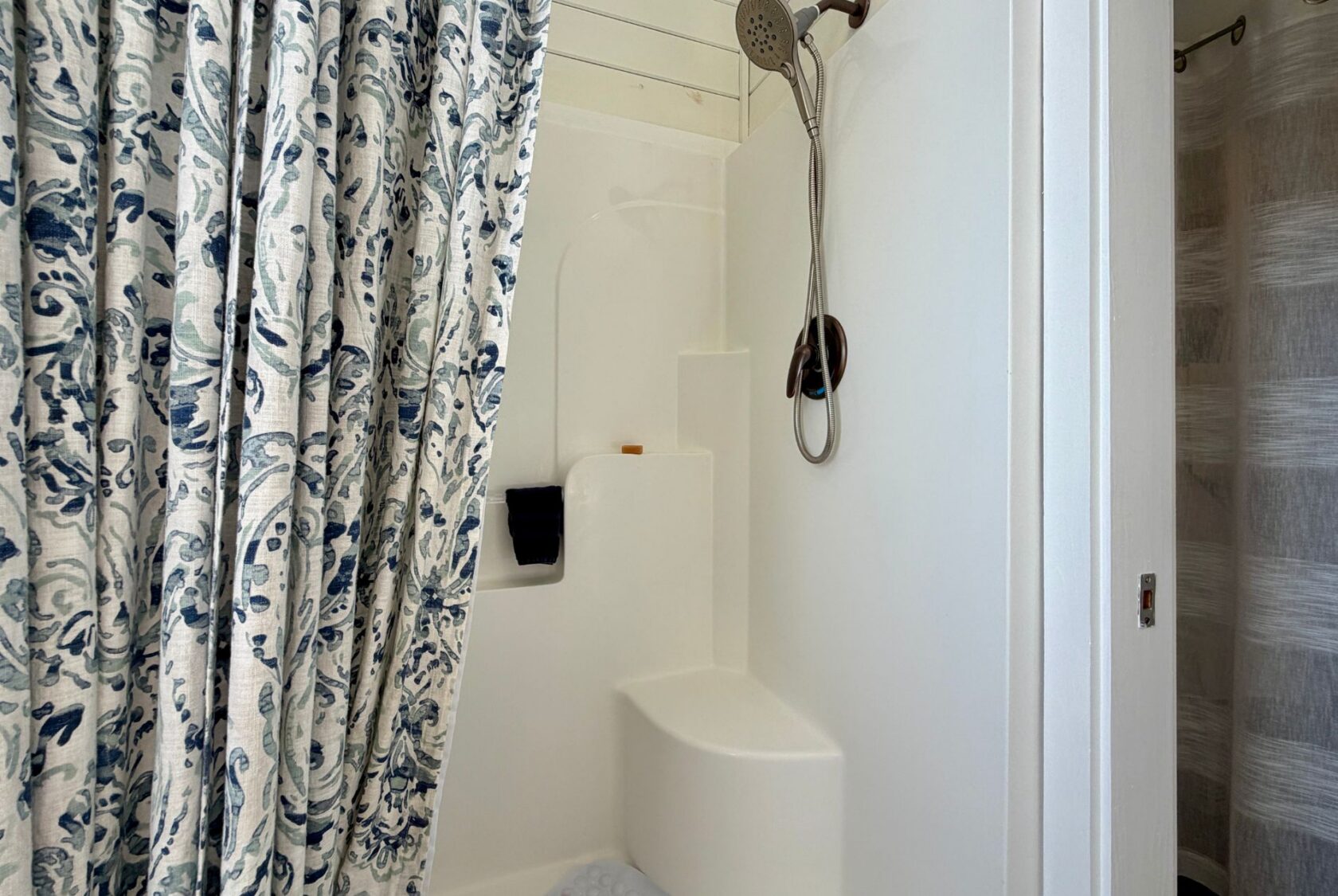 White shower with bench, bronze showerhead, and floral curtain partially open—a highlight of 47 Drifting Brook real estate.