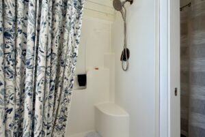White shower with bench, bronze showerhead, and floral curtain partially open—a highlight of 47 Drifting Brook real estate.