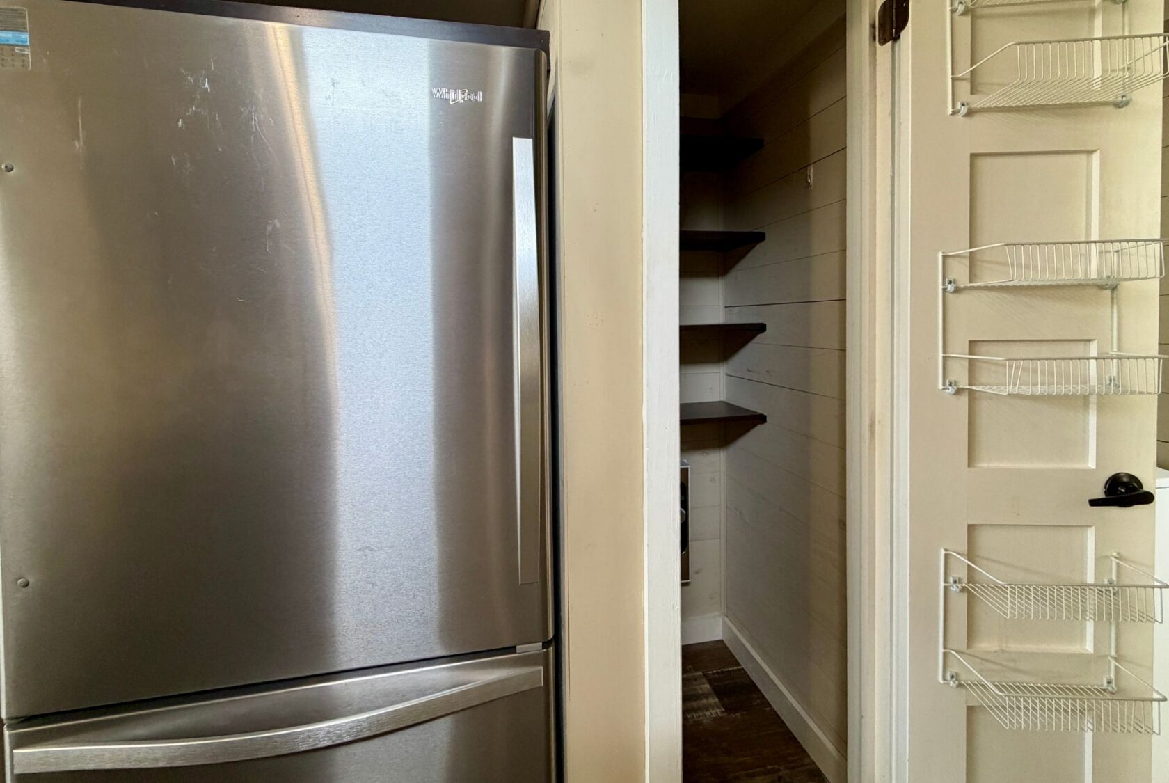 Stainless steel fridge beside a small pantry with shelves and door, located in Highland Hill Lane.