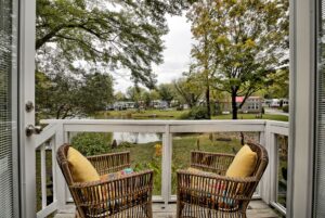 Two wicker chairs with yellow cushions on the balcony at 132 Drifting Brook overlook a peaceful pond and green trees.