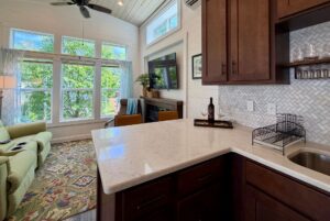 A cozy living room and kitchen at 59 Drifting Brook Lane features large windows, a green sofa, TV, and wine bottle on the counter.