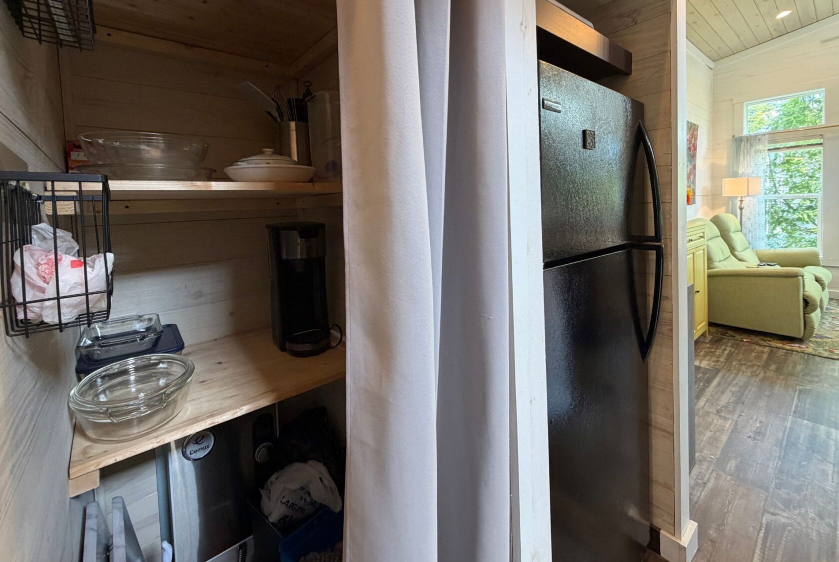 Small kitchen pantry with shelves, glass bowls, and black fridge; living room visible—ideal for real estate at 59 Drifting Brook.