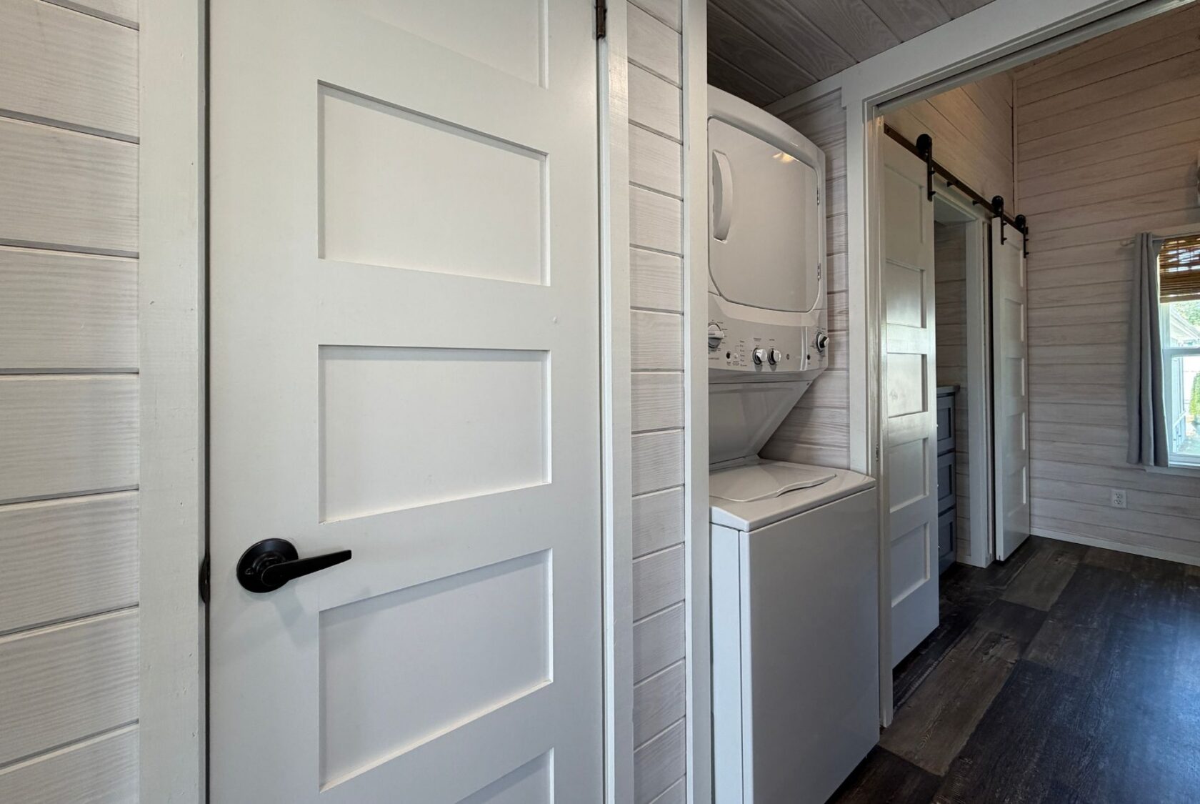 A stacked washer and dryer in a laundry nook near a white door, perfect for Strolling Easy Lane living.