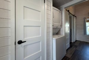 A stacked washer and dryer in a laundry nook near a white door, perfect for Strolling Easy Lane living.