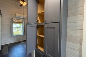 Tall gray cabinets with open doors line this Strolling Easy Lane-inspired room with wood panel walls and wooden shelves.