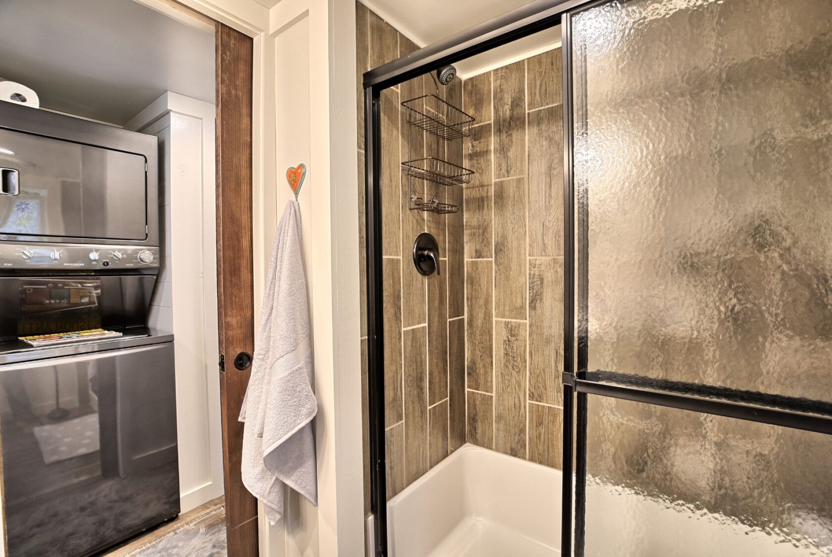 Modern bathroom at 132 Drifting Brook Lane with glass shower, towel on door, and stacked washer and dryer unit.