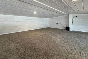 Cozy low-ceiling room on 15 Easy Lane with carpeted floor, white wooden walls, and recessed lighting.