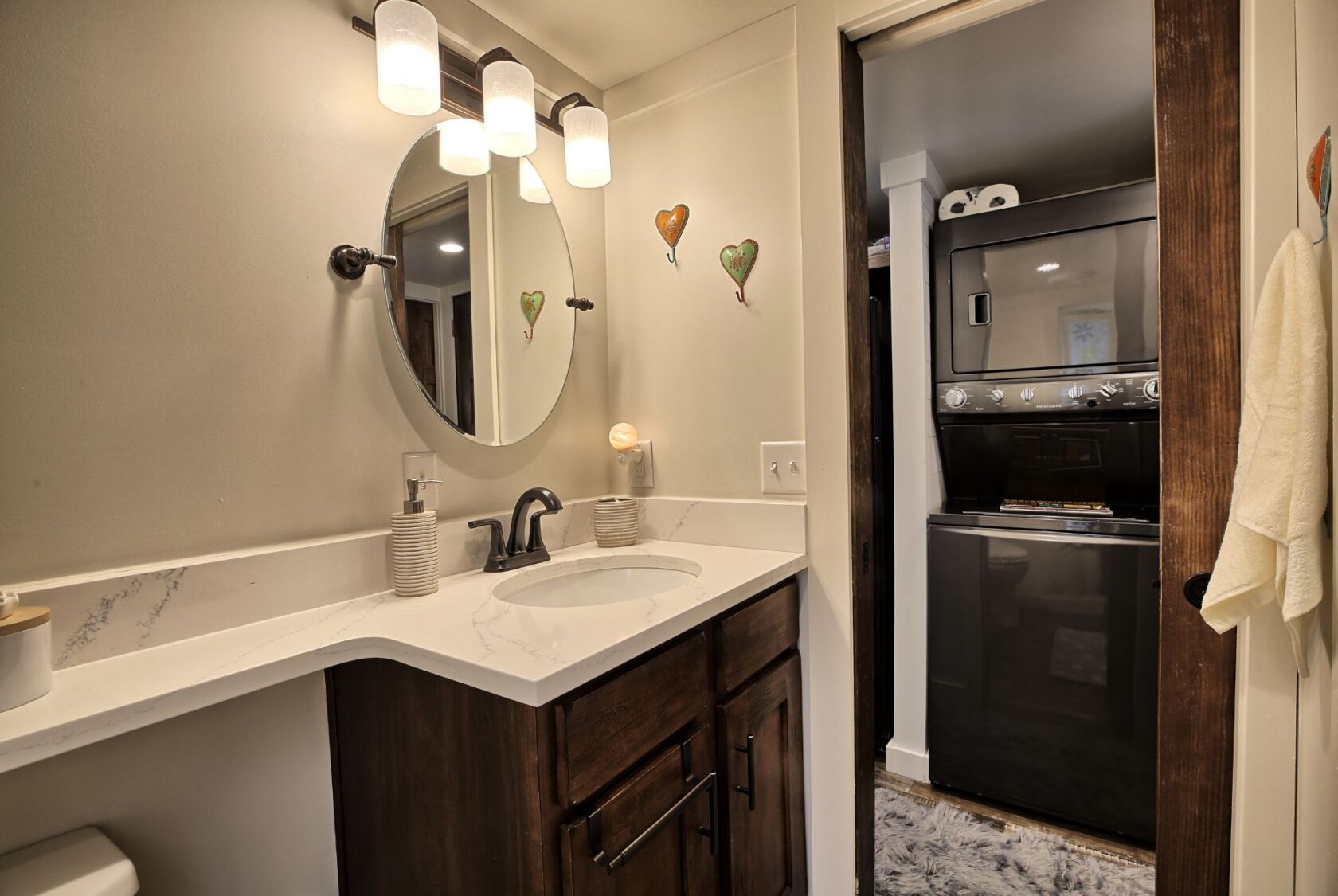 Modern bathroom with round mirror, vanity, and view of stacked washer and dryer at 132 Drifting Brook Lane.