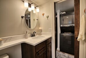 Modern bathroom with round mirror, vanity, and view of stacked washer and dryer at 132 Drifting Brook Lane.