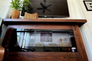 Wooden electric fireplace below a TV, with plants and baskets, in a cozy 59 Drifting Brook living room scene.