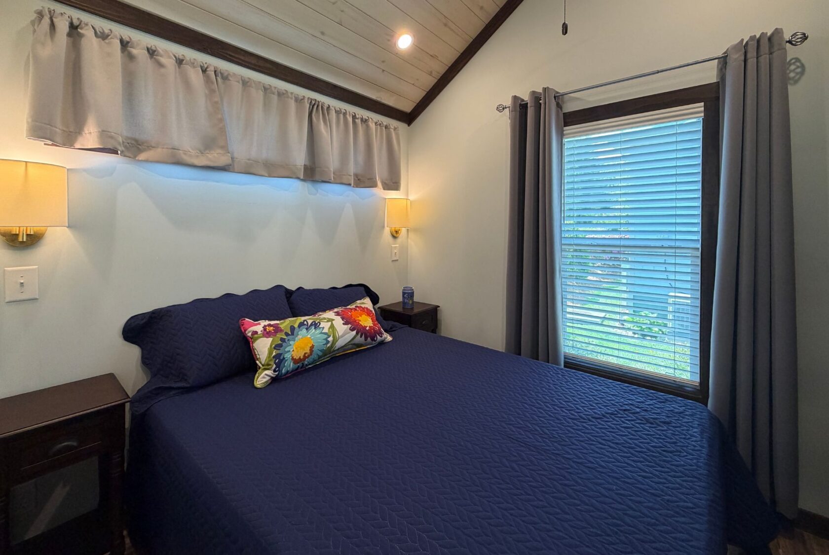 A cozy bedroom at 59 Drifting Brook with navy bedding, floral pillow, nightstands, and blue-gray curtains.