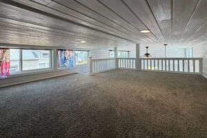 Loft with carpeted floor, white wood walls, colorful curtains, and a ceiling fan—ideal for Strolling Easy Lane living.