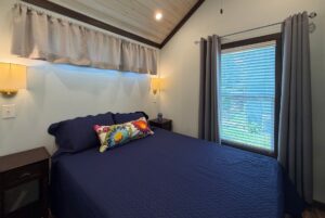 A cozy bedroom at 59 Drifting Brook with navy bedding, floral pillow, nightstands, and blue-gray curtains.