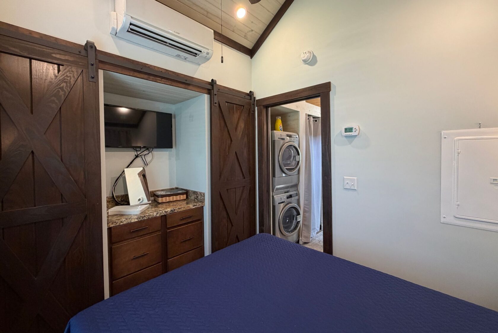 Bedroom at 59 Drifting Brook Lane features dark wood barn doors, TV, washer/dryer, and blue bedspread—ideal for real estate tours.