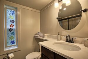 Modern bathroom at 132 Drifting Brook with round mirror, marble sink, stacked towels, and floral window—ideal real estate.